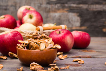 Sliced dried apples ready to eat in a bowl and fresh apples on a wooden tableの写真素材