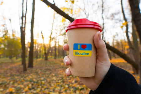 Ukraine. autumn evening. Sunset. city park. End of the working day. A cup of coffee with a patriotic sticker "I love Ukraine" in hand (close-up). Walks in the open airの写真素材