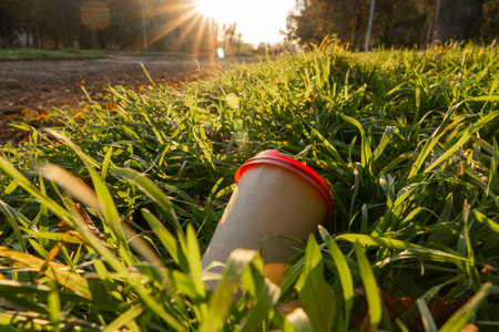 Evening. Sunset. Empty city street. End of the working day. A glass of coffee lies on a green lawn (close-up). Shooting from a lower levelの写真素材
