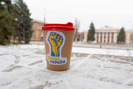 Winter. A cup of coffee with a patriotic sticker on the ground against the backdrop of a city street...