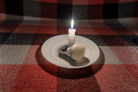 An LED light bulb lies near a burning candle (close-up). power outage concept. blackout. energy crisisの写真素材
