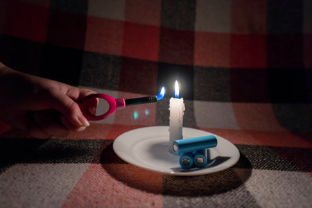 A woman lights a candle with a gas lighter. Near the candle are three discharged cylindrical batteries (close-up). power outage concept. blackout. energy crisisの写真素材