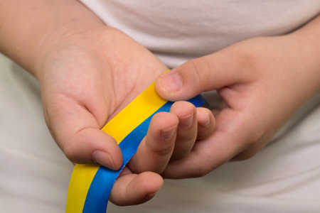 A girl in a white T-shirt holds a yellow-blue ribbon in her hands. State flag of Ukraine. National...