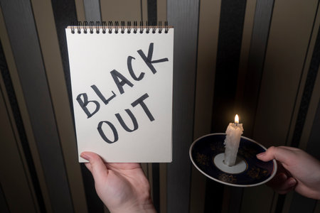 A notepad with the inscription Blackout in one hand and a burning candle in the other hand...