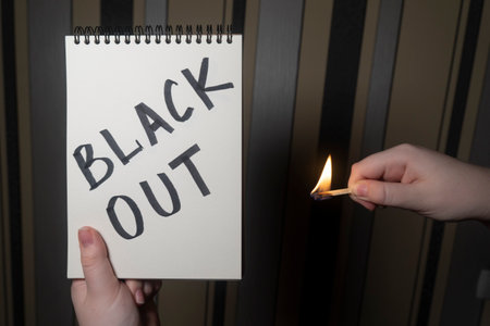 Notepad with the inscription "Blackout" in one hand and burning matches in the other hand (close-up). power outage concept. energy crisisの写真素材