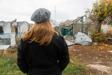 The girl looks at the house destroyed by shelling. War in Ukraine. Russian invasion of Ukraine. countryside. Terror of the civilian population. war crimesの写真素材