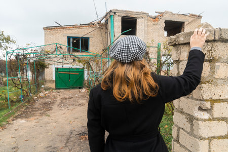 The girl looks at the house destroyed by shelling. War in Ukraine. Russian invasion of Ukraine. countryside. Terror of the civilian population. war crimesの写真素材