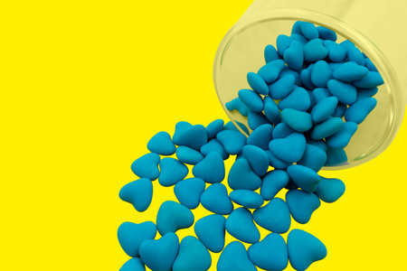 Overturned glass with blue heart shaped candies (close-up) isolated on yellow background. State symbols of Ukraine. View from aboveの写真素材