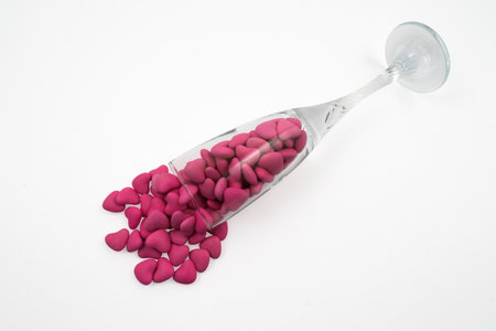 Overturned glass with heart shaped pink candies (close-up) isolated on white background. View from...