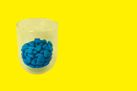 Glass with blue heart shaped candies (close-up) isolated on yellow background. View from above
