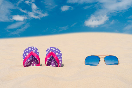 Blue sunglasses and flip flops lie in the sand against the blue sky. Summer vacation, travel and tourism concept. Summer rest. holiday seasonの写真素材
