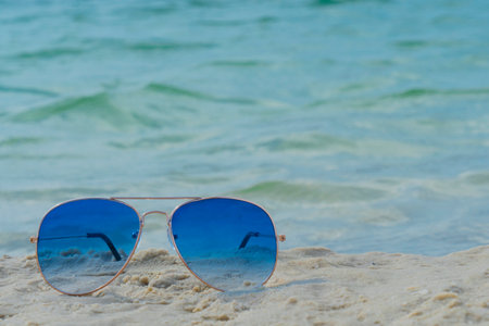 Blue sunglasses lie in the sand on the beach near the sea. Summer vacation, travel and tourism concept. Summer rest. Vacation season.の写真素材