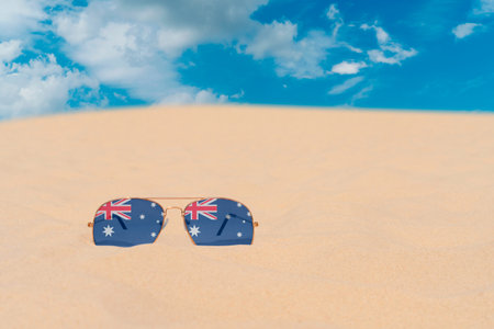 Sunglasses with glasses in the form of the flag of Australia lie on the sand against the blue sky. The concept of summer holidays, travel and tourism in Australia. summer restの写真素材