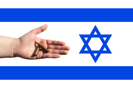 Two rifle cartridges in the palm against the background of the Israeli flag. Israeli-Palestinian conflict. Terror of civiliansの写真素材