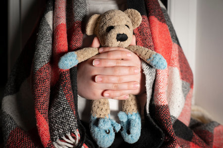 Blackout. Children's toy (teddy bear) in hands close-up. Power outages, destruction of energy infrastructure. Terror of civiliansの写真素材