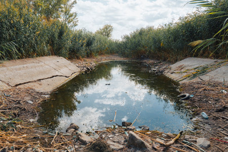 A drying irrigation canal on a cloudy summer day. Conceptual representation of climate change, drought and drying up of water bodiesの写真素材