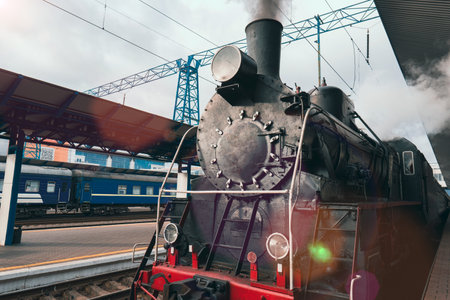 An old vintage steam locomotive is preparing to depart from the platform of a railway station. The historical era of steam enginesの写真素材