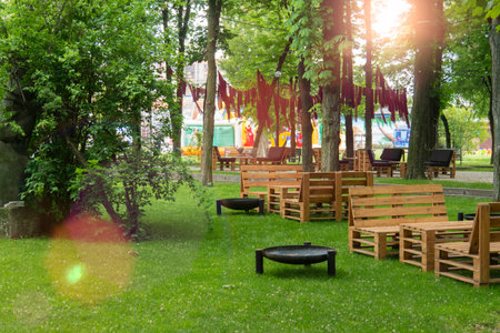 Cozy outdoor lounge and dining area in a green park with handmade rustic wooden pallet furniture and fire pits under the canopy of treesの写真素材