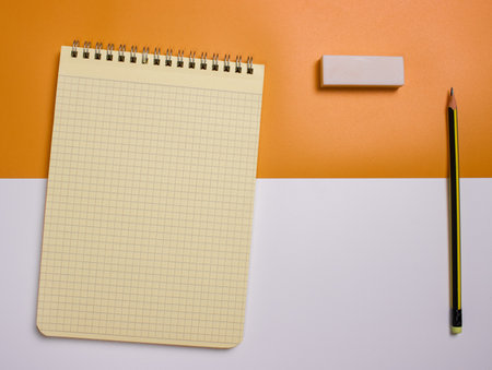 Top view of an open notebook with a pencil and an eraser on a white and yellow background. School...