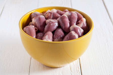 Raw chicken hearts in a yellow bowl on a white wooden table. In the center of the frame.の写真素材