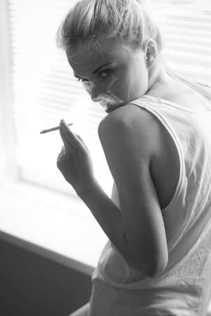 beautiful young woman smokes at home by the windowの写真素材