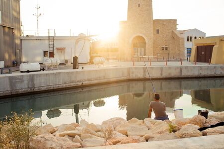 Man fishing on a lake from the stone embarkment at sunset in Limassol, Cyprus. Colorful horizontal...