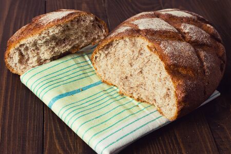Close up of fresh and tasty loaf of whole wheat bread laying in green white napkin with stripes on...