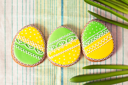 Easter homemade gingerbread cookie and yellow end green eggs over grenn and white cloth. Colorful...