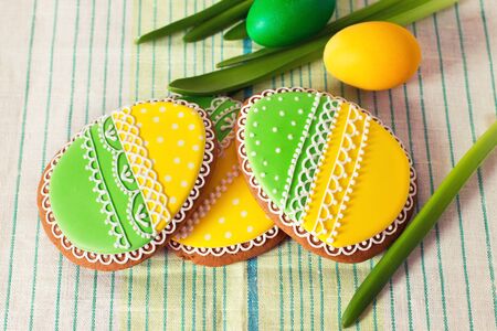 Easter homemade gingerbread cookie and yellow end green eggs over cloth. Colorful image, top view