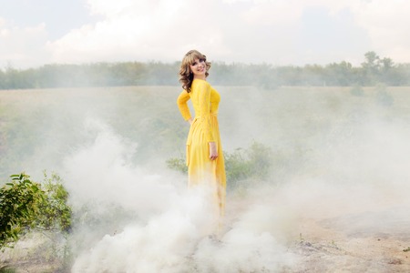 Outdoor portrait of a beautiful brown hair woman in yellow dress. Attractive girl in the fog from smoke pot. Horizontal photo.の写真素材