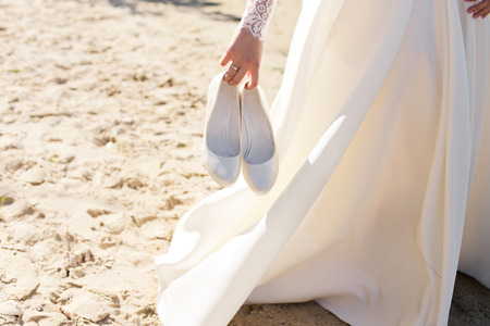 Wedding warm white shoes in brides hands on the beach.の写真素材