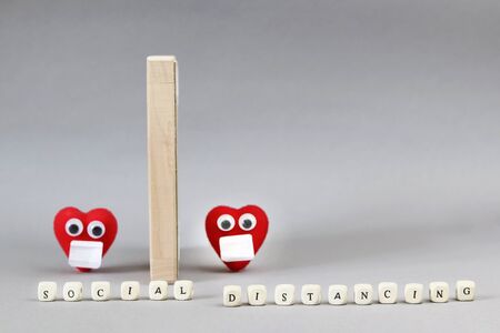 Words of social distance from cubes. Defocused two red hearts with eyes and masks and a wooden partition. Copy space - the concept of prevention, quarantine, security, the spread of coronavirusの写真素材
