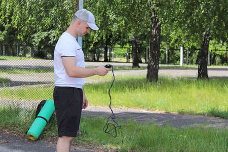 A young guy holds a black rope in a park in sunny, summer weather. Copy space - sport concept,...