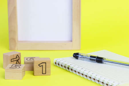 Numbers written on wooden cubes. Defocused wooden frame for text and a black pen on a white notepad....