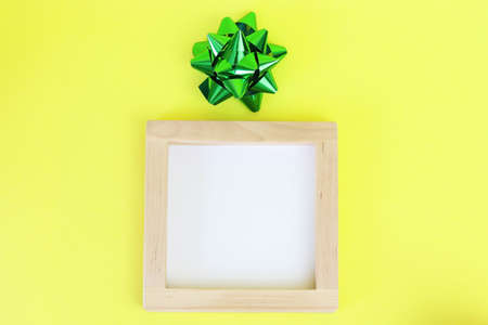 Wooden frame and green bow. Colorful, yellow background for text. Copy space - holidays concept,...
