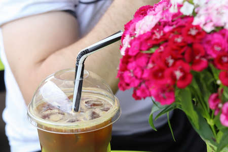 A refreshing, coffee cocktail with ice. Defocused bouquet of Chinese carnations on a table in a street cafe. Copy space - summer concept, flowers, walk, drinks, warm.の写真素材