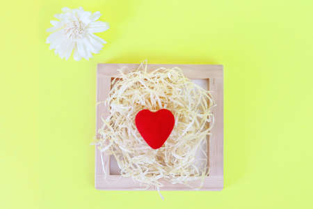 Red heart. Defocused cardboard, organic box filled with shredded paper on a yellow background top view. Holiday card. Copy space - concept of environmental packaging for gifts for a birthday, wedding.の写真素材