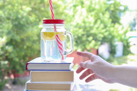 A refreshing, lemon cocktail on a stack of books on a background of tree leaves. Copy space -...