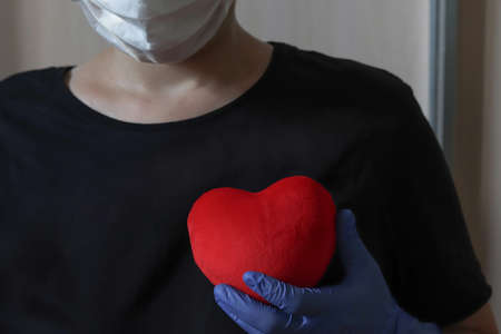 A nurse in a medical mask and gloves holds a red heart.の写真素材