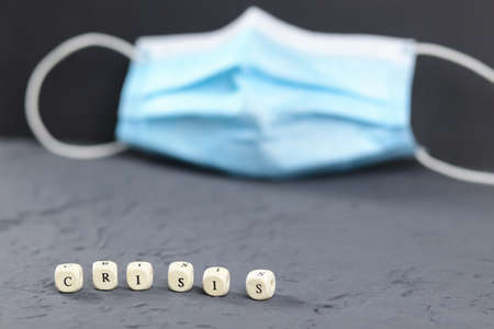 The word crisis, which is assembled from cubes in the foreground and a blurry medical mask. Copy space - financial concept, world economic problems.の写真素材