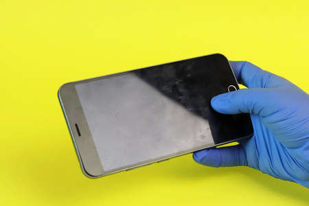Hand in a medical glove and dirt on the surface of a smartphone. Copy space - equipment cleaning...