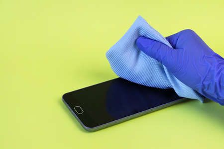 A hand in a medical glove with a microfiber disinfectant cloth wipes dirt from the surface of a smartphone. Copy space - equipment cleaning concept, cleanliness, spread of coronavirus, prevention.の写真素材