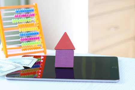 House of wooden figures. Defocused tablet, dollars and banknotes. Copy space - the concept of paying...