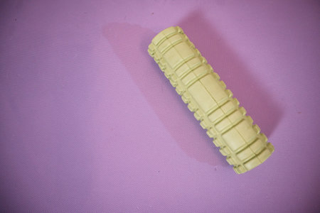Foam roller lying on its side on a vibrant purple background, with empty space for text. Minimalist fitness and recovery concept.の写真素材