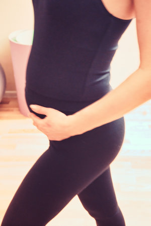 A pregnant woman in fitness clothing gently embracing her belly, symbolizing motherhood, self-care, and a healthy pregnancy lifestyle.の写真素材
