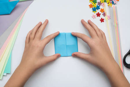 children's hands do origami on a table. Nearby sheets of color paper lie.の写真素材