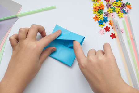 children's hands do origami on a table. Nearby sheets of color paper lie.の写真素材