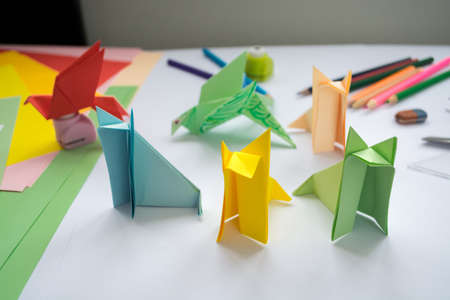 Children's  origami  wolf's and bird's from colored paper. Working place is decorated with leaves of color paper, scissors, colored wood ladybugs and pencils.の写真素材