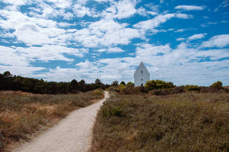 a road to the white church over the background of the blue sky and white clouds. Sanded Church,...