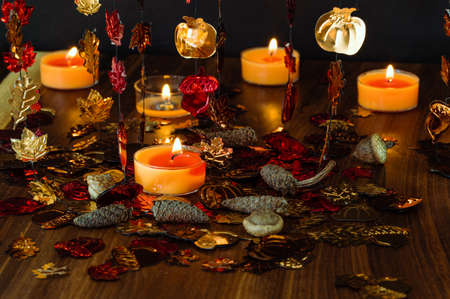 Horizontal photo of an artificial autumnal leaves, burning orange candles and dried acorns and cons over the dark backgroundの写真素材